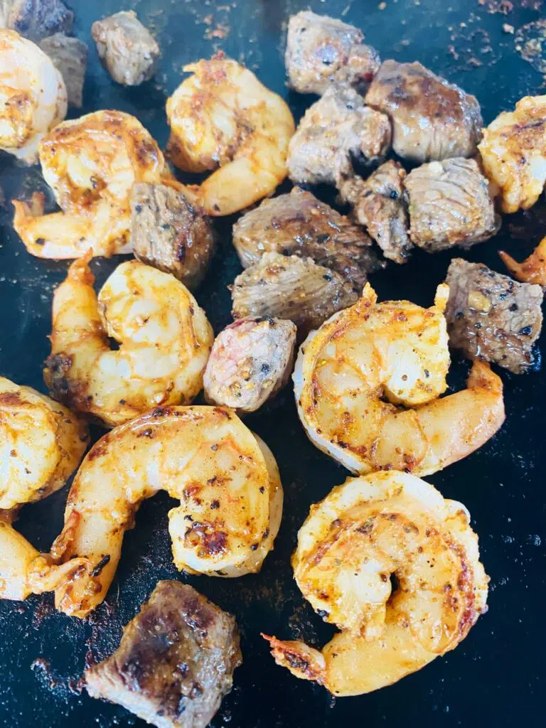 shrimp and steak cooking on the griddle
