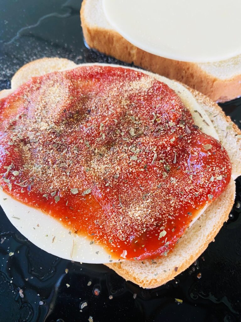 adding pizza sauce and seasoning to the sandwich