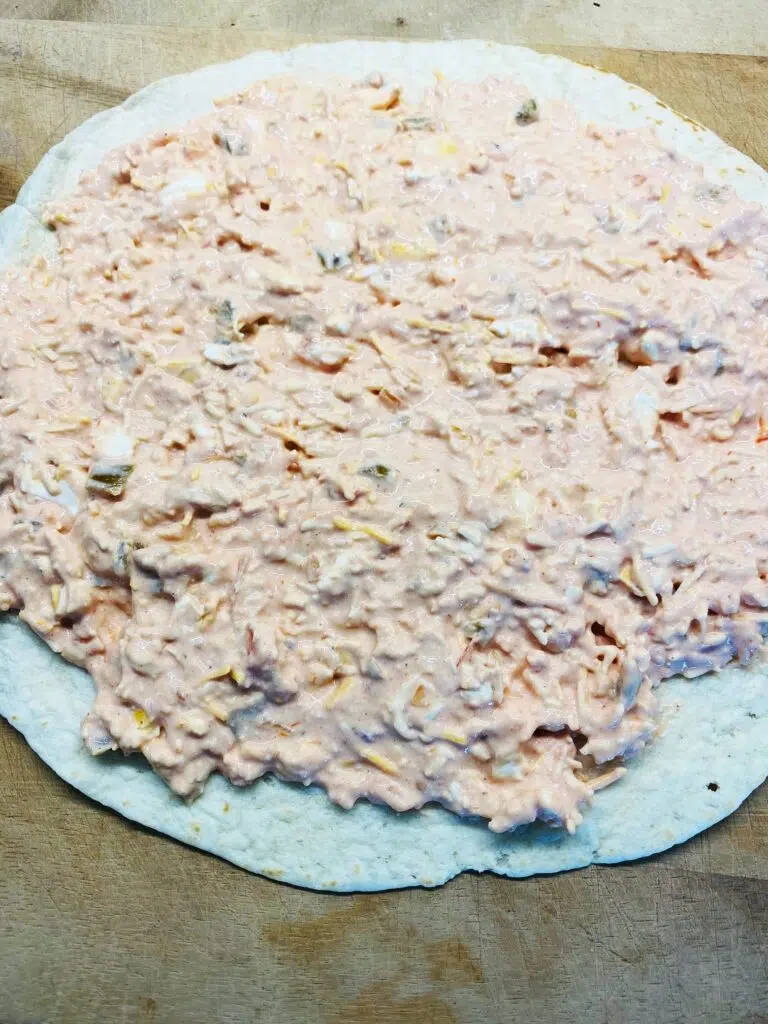 spreading the cheesy filling over a tortilla for Smoked Cheesy Salsa Pinwheels