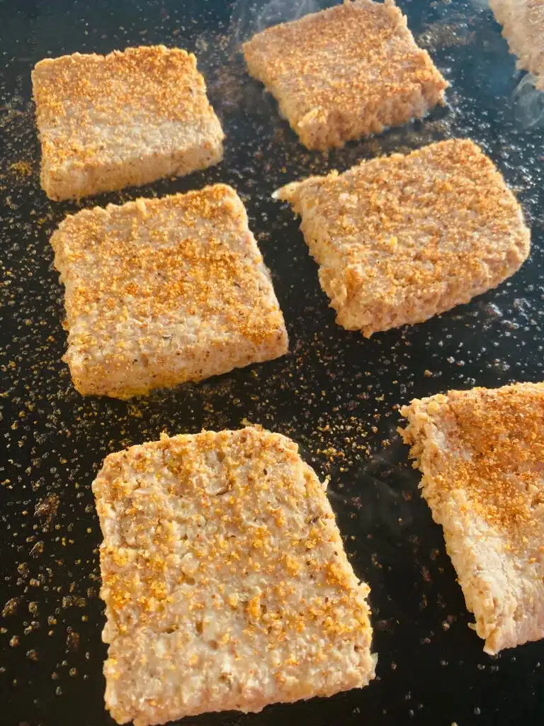Goetta on the griddle with Cajun seasoning before cooking