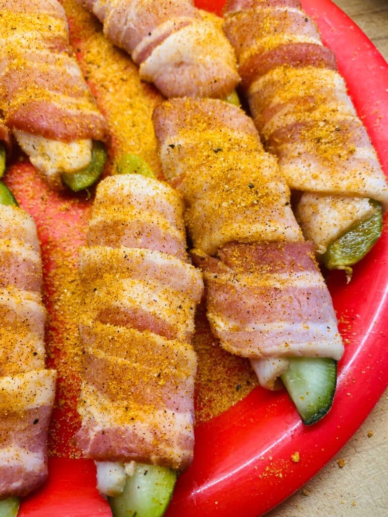 Pickles wrapped in bacon before cooking seasoned with BBQ seasoning
