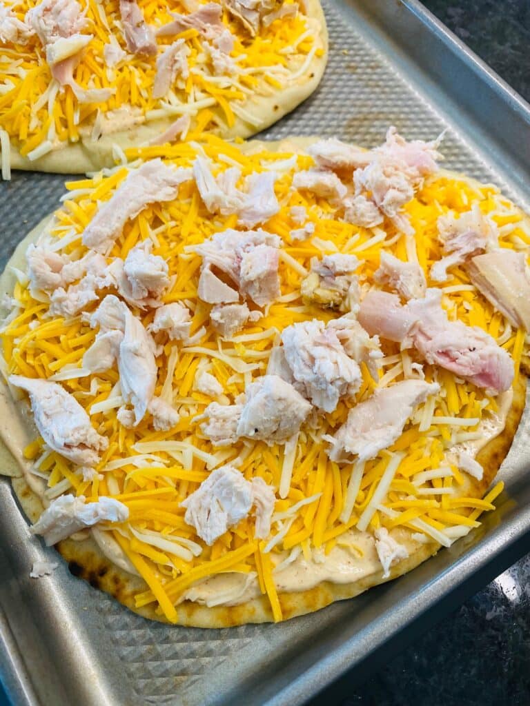 adding cheese and chicken to the pizza crust