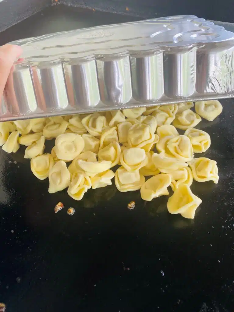 tortellini cooking on the griddle with a melting dome