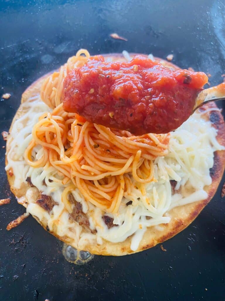 adding more sauce to Blackstone Smashed Spaghetti Tacos