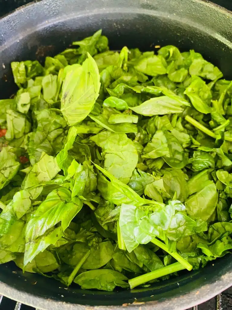 adding spinach and basil to the sauce before stirring