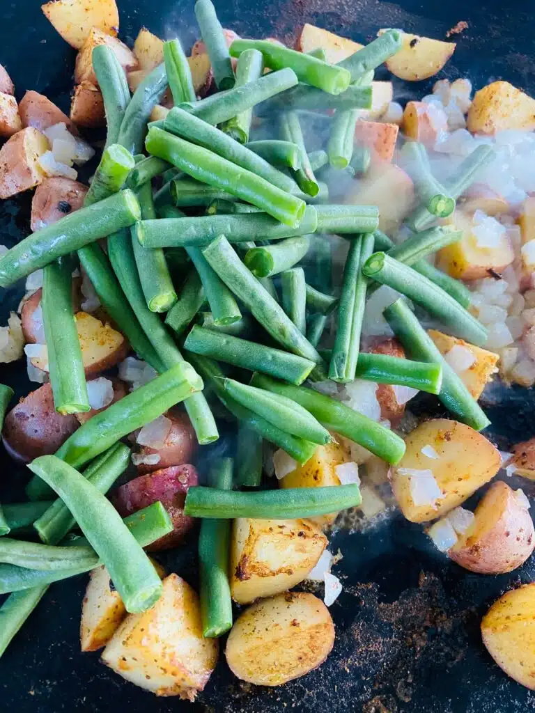 adding onions and green beans to the griddle