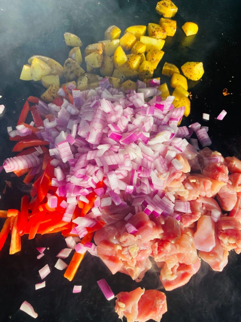 adding onions and peppers and chicken to the griddle