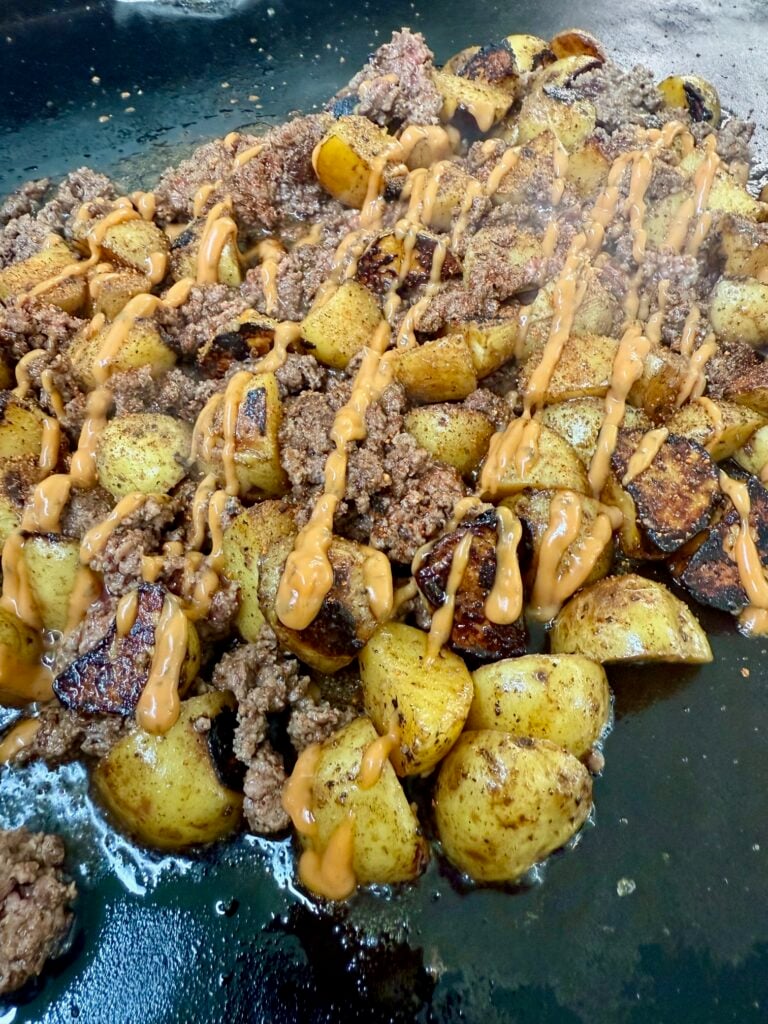 adding burger sauce to Blackstone Cheesy Potato Burger Bowls