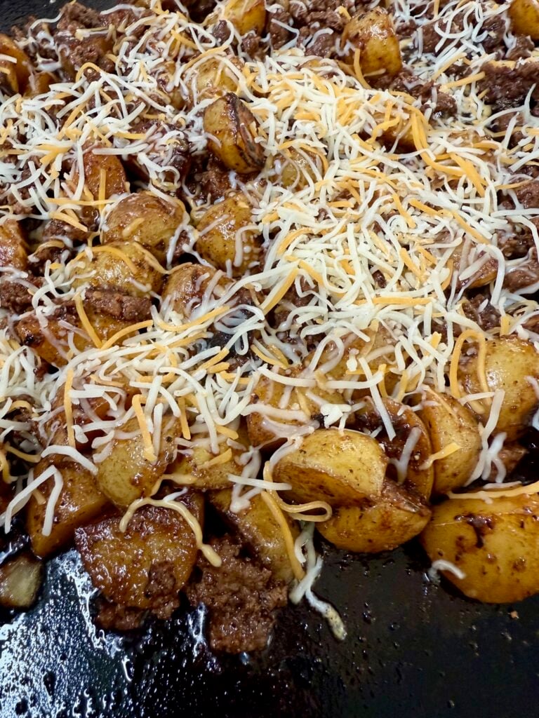 adding cheese to Blackstone Cheesy Potato Burger Bowls