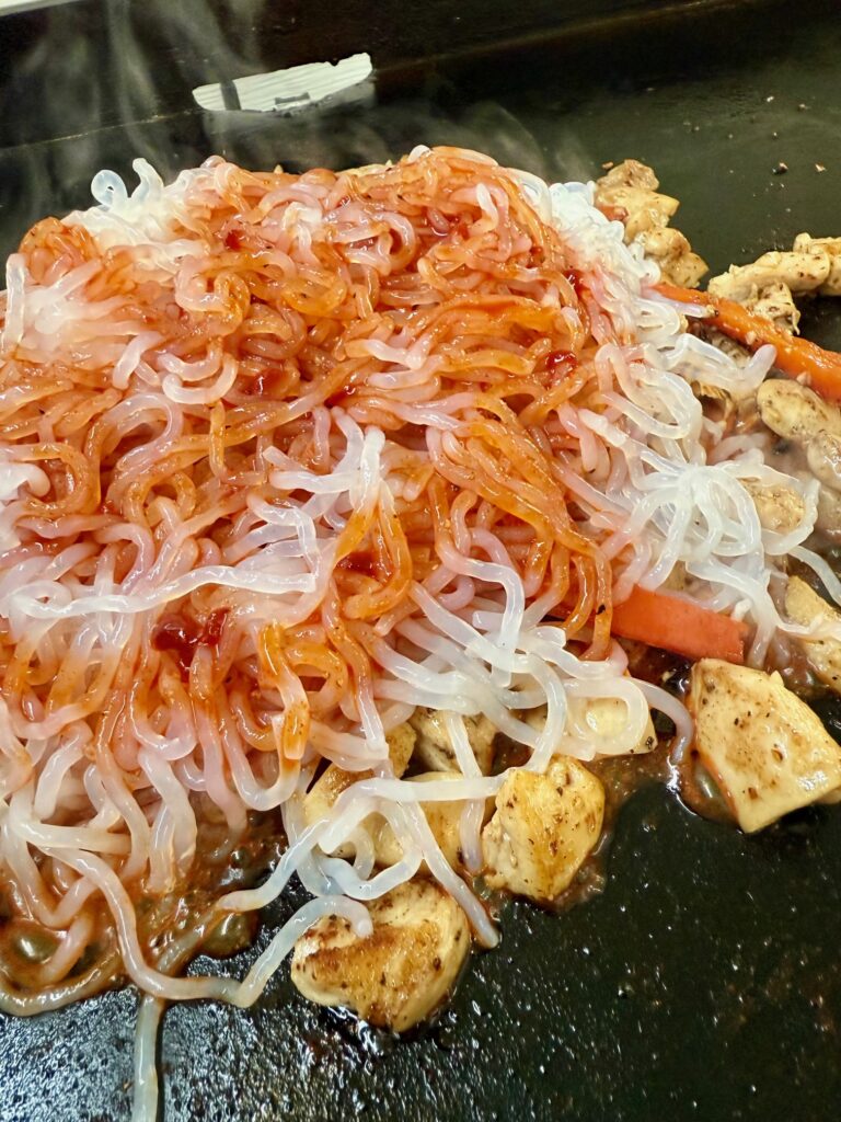 adding sauce and noodles to Blackstone Low Carb Korean Chicken Noodles