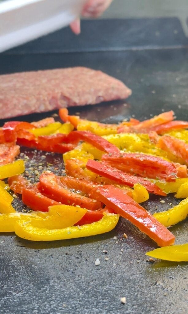 peppers and sausage cooking on griddle
